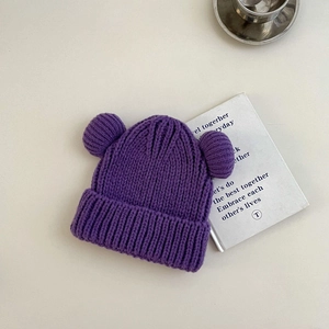 Close-up of a purple knitted kids hat featuring dual pom-poms and thick wave texture