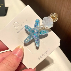 Detail view of starfish hair clip with blue sequins, pearls and shell on display card
