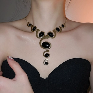 Detail of gold necklace with black oval stones shown on a model against a black top