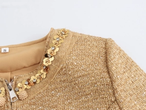 Close-up of beige tweed jacket neckline featuring golden sequins and rhinestone trim detail