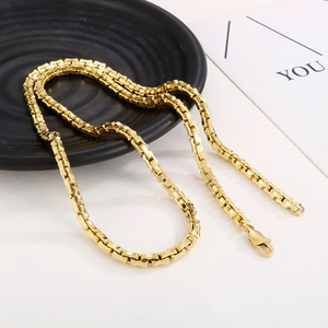 Detailed view of polished gold box chain with lobster clasp on a textured display