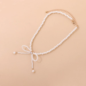 Macro detail of pearl necklace featuring a sparkling crystal bow and gold lobster clasp