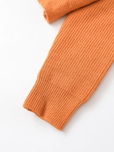 Dettaglio dei polsini di un maglione in maglia arancione con trama a coste verticali