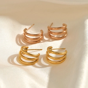 Three-layer C-shaped gold and rose gold hoop earrings on beige silk fabric