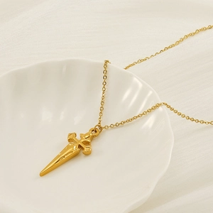 Detailed view of a gold cross sword pendant necklace displayed on a white shell plate