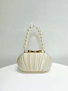 Detalle del elegante bolso de fiesta en satén plisado con asa de perlas y lazo dorado