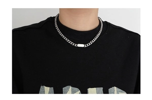 Detail of silver Cuban chain necklace with rectangular pendant worn over a black hoodie