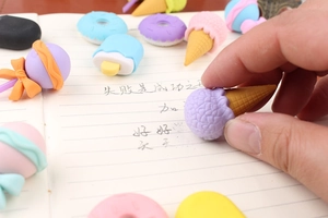 Close-up of hand picking a purple ice cream shaped eraser over an open notebook