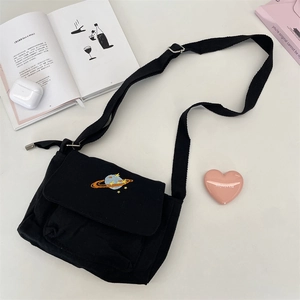 Flat lay of black canvas messenger bag featuring planet embroidery and lifestyle items