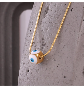 Detailaufnahme der goldenen Schlangenkette mit weißem Emaille-Anhänger im Evil-Eye-Design