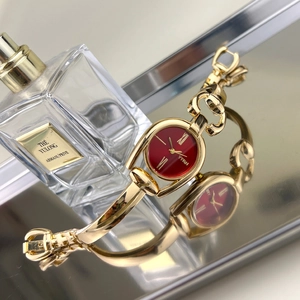 Detail shot of the golden horsebit bracelet watch featuring a dark red sunray dial
