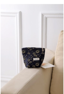 Close-up of a navy blue canvas makeup bag with gold floral embroidery on a sofa