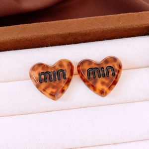 Close-up of tortoise shell heart stud earrings with black branding in a white box