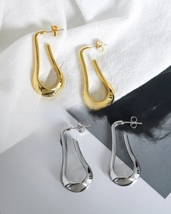 Polished gold and silver U-shaped drop earrings shown against a fashion magazine