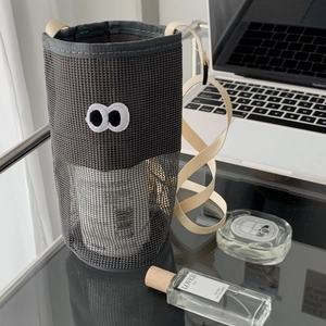 Detail of dark grey mesh bag with cartoon eyes on a desk with lifestyle accessories