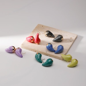 Colorful resin teardrop earrings set with gold-tone studs on a beige stone slab