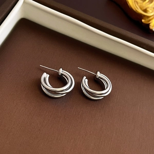 Close-up of triple-layered silver geometric C-shape earrings on a dark matte surface