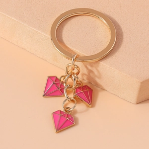 Close-up of golden keychain with three pink diamond-shaped enamel charms on steps