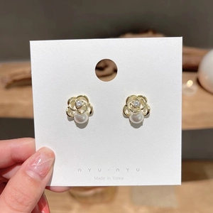 Macro shot of gold hollow flower earrings featuring zircon and pearl on a white card