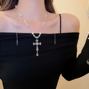Close-up of a silver cross pendant necklace with rhinestones and pearls on a model