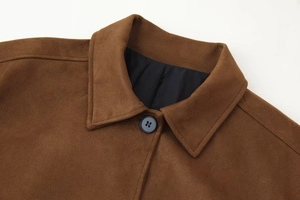 Detail of brown suede jacket showing lapel collar, black buttons, and fabric texture