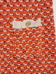 Detail of orange and white textured knit fabric with gold crest button and white trim