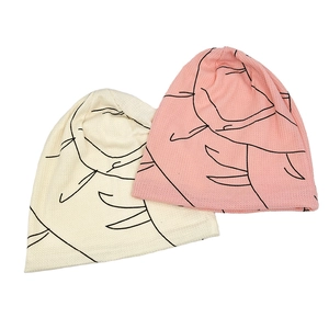 Flat lay detail of cream and pink knitted slouchy beanies with abstract line prints