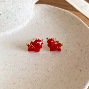 Close-up of red and gold enamel flying pig stud earrings on a beige ceramic tray