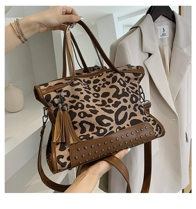 Detail of leopard print tote bag featuring brown leather trim, metal rivets and fringe tassel