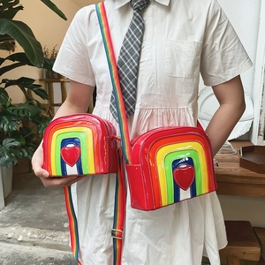 Detail of rainbow striped patent leather crossbody bags with heart accent and woven strap