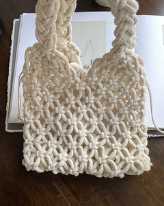Close-up of cream white hand-woven cotton bag with floral texture on wood surface