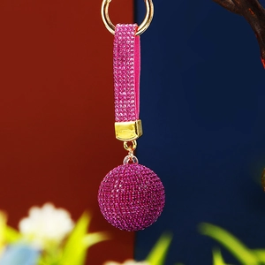 Detail of pink rhinestone keychain ball with golden metal ring on blurred background