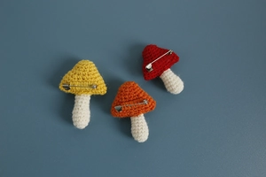 Detailed view of three handmade crochet mushroom brooches in yellow, orange, and red colors