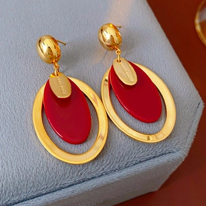 Macro detail of gold-plated earrings with red resin charms and Hand Made engraving