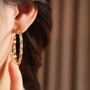 Close-up of golden geometric C-shape earrings with diamond-cut texture on model