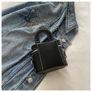Détail du mini sac boîte noir avec coutures blanches et chaîne argentée sur du denim