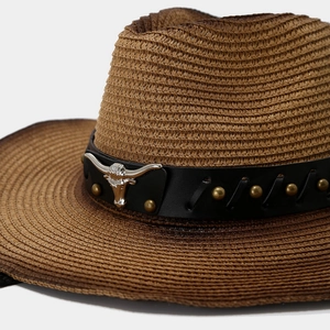 Brown woven cowboy hat with leather band and silver bull head emblem on white background