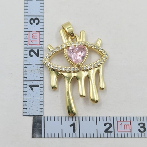Detail view of gold Evil Eye pendant with pink heart gemstone and size reference scale