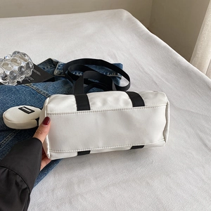 White nylon Boston barrel bag with black handles and round coin purse on denim