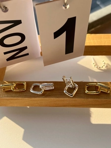 Close-up of geometric U-shaped gold and silver earrings on a minimalist wooden stand
