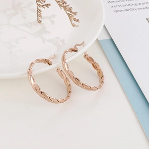 Close-up of twisted rope gold hoop earrings on a decorative white porcelain tray