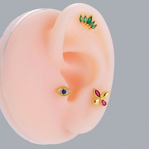 Dettaglio di tre orecchini a perno con marquise verde, occhio greco e design a fiocco rosa