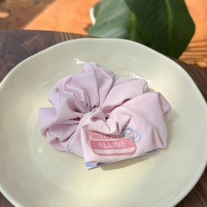 Close-up of a pink fabric scrunchie with a creative Hello my name is brand tag detail