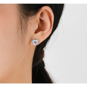 Close-up of heart-shaped silver earring with pink gemstone and blue enamel details