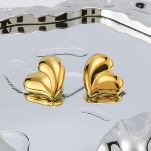 Polished 18K gold plated heart stud earrings on a metallic tray with water droplets