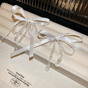 Elegant white silk bow earrings with transparent beaded tassels on a jewelry stand