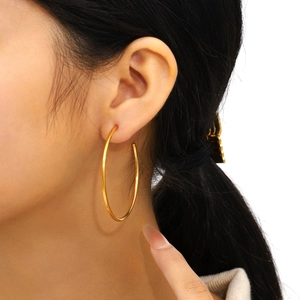 Close-up of a model wearing large polished gold C-shaped hoop earrings in a minimalist style