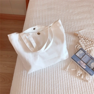 Detail of white cotton canvas tote bag with metal magnetic clasp on a white quilted surface