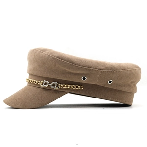 Detail of khaki military cap featuring golden chain and sparkling rhinestone buckle