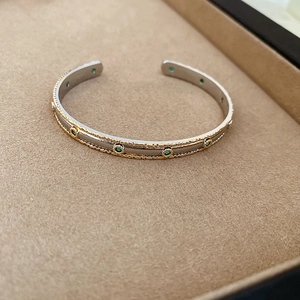 Vue détaillée d'un bracelet ouvert bicolore avec pierres vertes et bordures perlées d'or